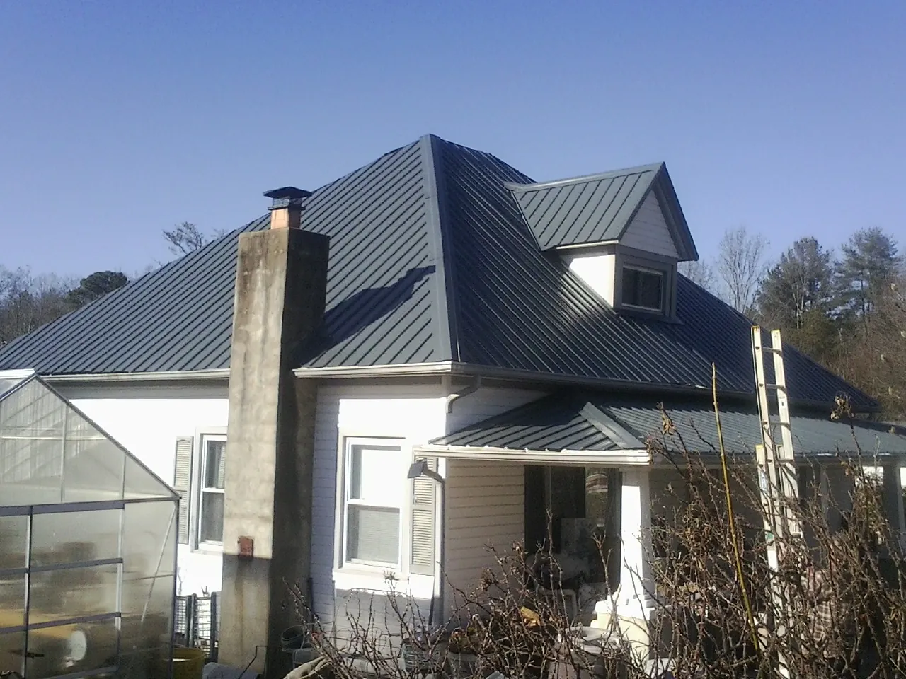 Dark blue standing seam metal roof on a white farmhouse with dormer — Slate & Tile Roof Repair by Roofing Brothers in Oliver Springs