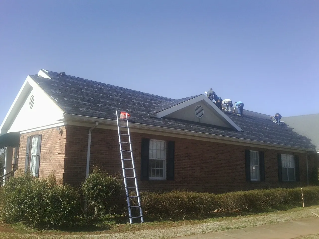 Crew tearing shingles off a brick ranch roof with a ladder set — Emergency Roof Repair work by our crew in Oliver Springs