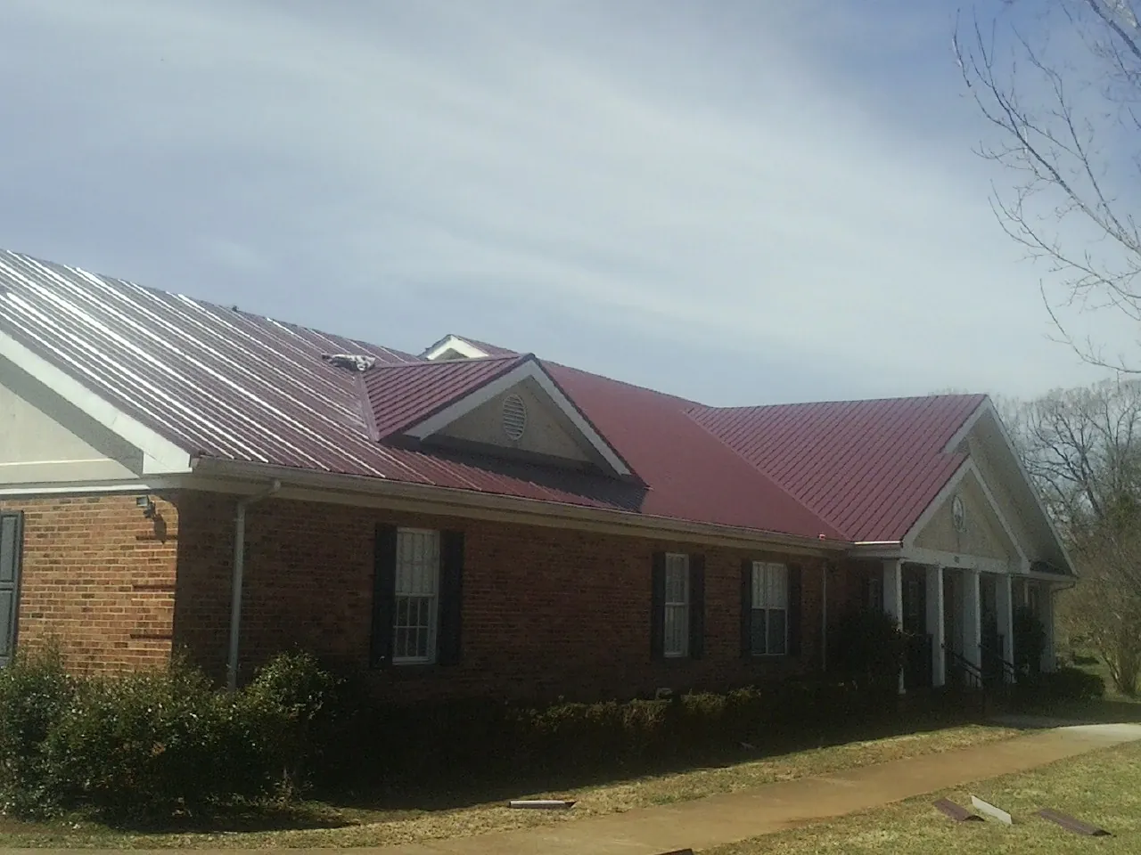 Red metal roof with gabled entries on a long brick building, from a Hail Damage Roof Repair job in Oliver Springs
