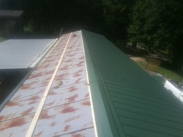 Old rusted panels beside newly installed green metal roofing — Wind Damage Roof Repair by Roofing Brothers in Oliver Springs