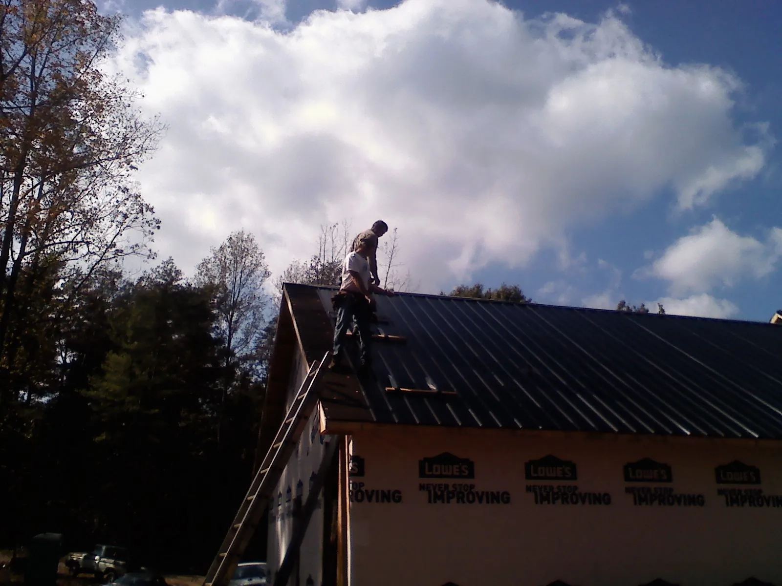 Roofer fastening dark metal panels high against a cloudy sky, from a Roof Inspection job in Oliver Springs