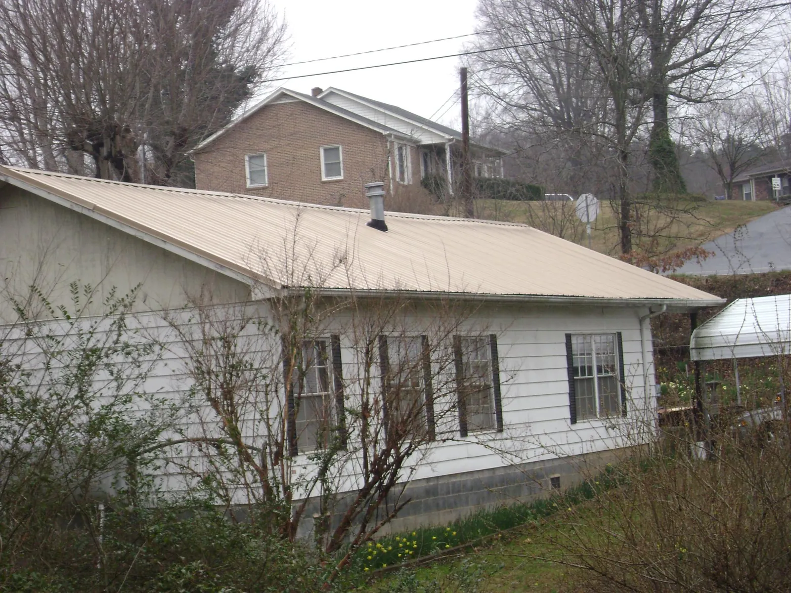 Tan metal roof on a white sided house set into a hillside — Commercial Roofing by Roofing Brothers in Oliver Springs
