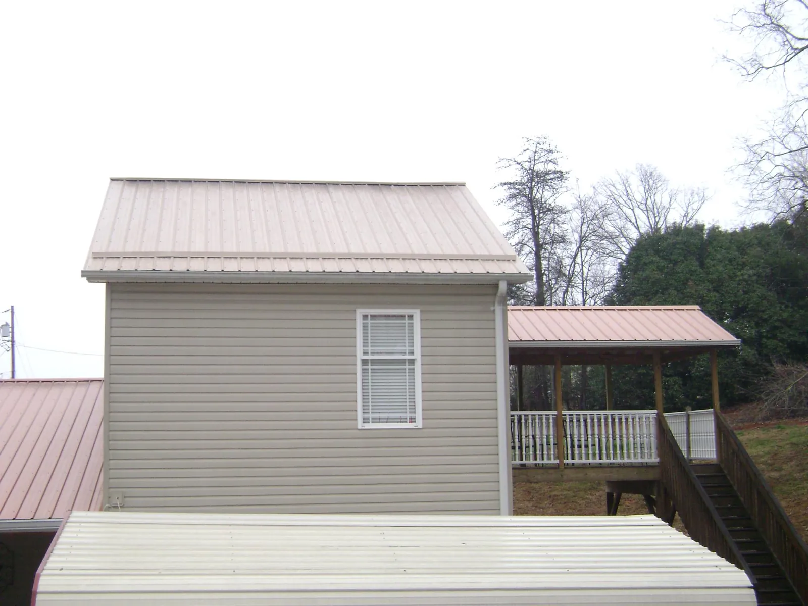 Tan metal roofs on a two story addition and attached porch, from a Roof Replacement job in Oliver Springs